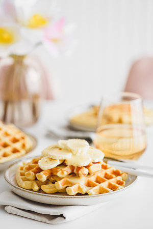 Belgian waffles with banana and condensed milk on white tableの写真素材