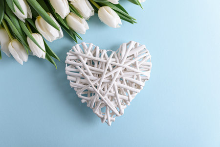 Floral border from bouquet of white tulips and wooden heart on blue background. Anniversary celebration concept. Top viewの写真素材
