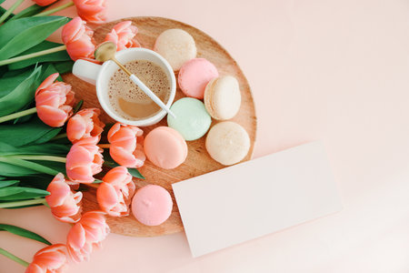 Bouquet of pink tulips, cup of coffee and macaroons on pink background. Anniversary celebration concept. Copy space. Top viewの写真素材