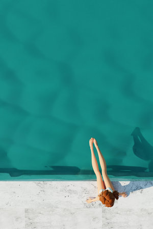 Young girl with in bikini sunbathing by swimming pool. Summer swimming pool party. 3d render. Top viewの写真素材