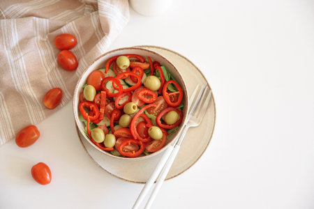 Healthy vegetarian salad with fresh cherry tomato, cucumber, sweet pepper, green olives and lettuce in bowl on white table. Top viewの写真素材