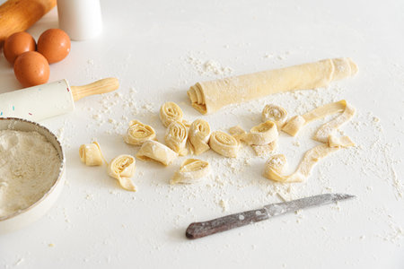 Preparing homemade tagliatelle pasta on on white table: cutted roll of dough. Top view