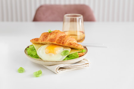 Croissant toast with lettuce, cheese and fried egg on white table.の写真素材