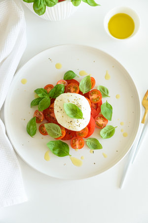 Salad Caprese with tomato, cherry, mozzarella and basil leaves on white wooden tableの写真素材