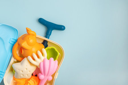 Colorful and playful summer kids beach suitcase with molds and toys on blue background. Top view. Copy spaceの写真素材