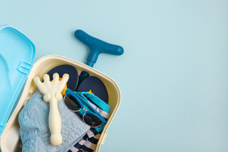 Colorful and playful summer kids beach suitcase with molds, jeans hat, and sunglasses on blue background. Top view. Copy spaceの写真素材