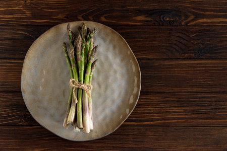 Asparagus tied bundle on brown plate on rustic table. Top viewの写真素材