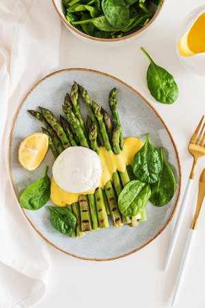 Poached egg with grilled asparagus, spinach, and hollandaise sauce on white table. Top viewの写真素材