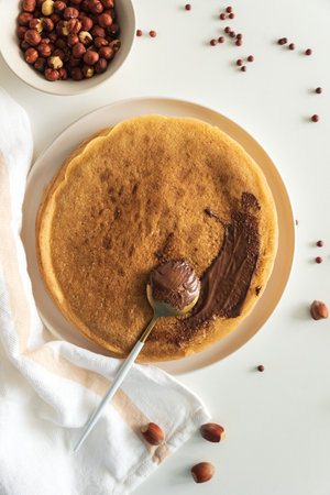 Crepes with chocolate hazelnut spread, strawberries and hazelnuts on a white wooden table. Top viewの写真素材