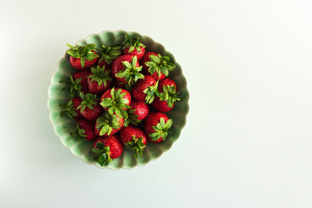 Fresh red strawberries in a green bowl on white table. Top viewの写真素材