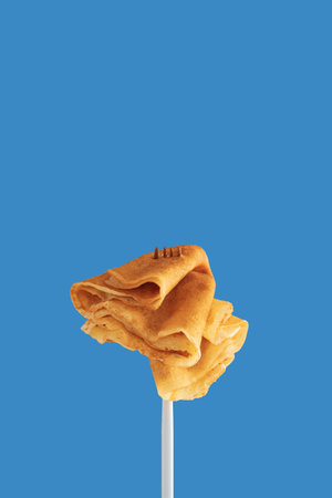 Golden pancakes on a fork against a vibrant blue background.の写真素材