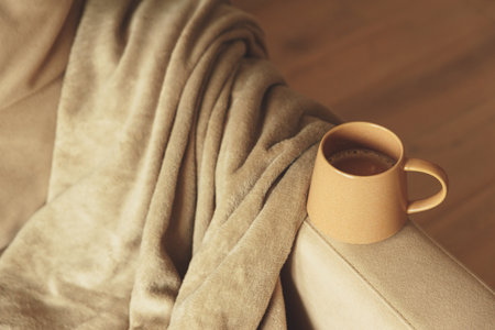 Mug of hot coffee stay on arm of chair by blanketの写真素材