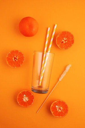 Preparing lemonade. Oranges, straws, and a glass on a vibrant orange background.の写真素材