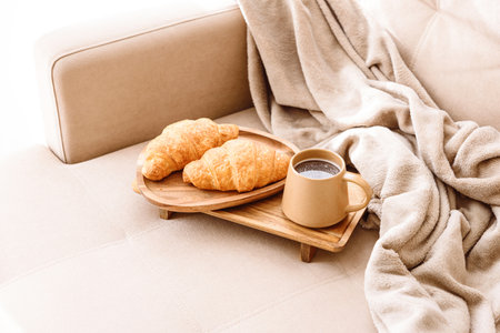 Coffee and croissants served on a wooden tray on a beige couch. Soft focusの写真素材