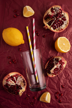 Preparing lemonade. Pomegranates, lemons, straws, and a glass on a red background.の写真素材
