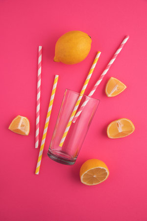 Preparing lemonade. Lemons, straws, and a glass on a vibrant pink background.の写真素材