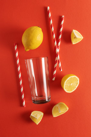 Preparing lemonade. Lemons, straws, and a glass on a vibrant red background.の写真素材