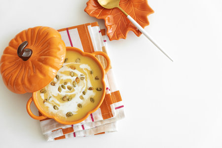 Autumn pumpkin soup in a pumpkin-shaped bowl on white tableの写真素材