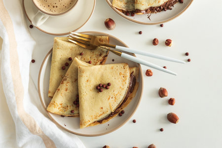 Crepes with chocolate hazelnut spread, strawberries and hazelnuts on a white wooden table. Top view