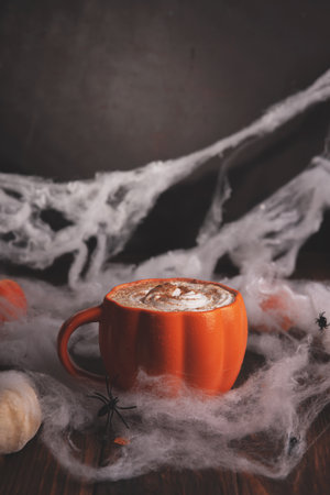 Halloween pumpkin latte with whipped cream and spooky decor on a wooden background.の写真素材
