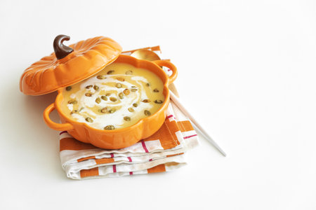 Autumn pumpkin soup in a pumpkin-shaped bowl on white tableの写真素材