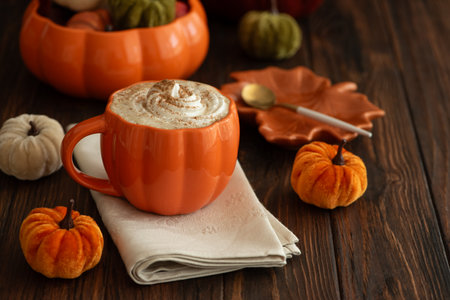 Cozy pumpkin latte in a pumpkin-shaped mug with whipped cream and spices, surrounded by autumn decor.の写真素材
