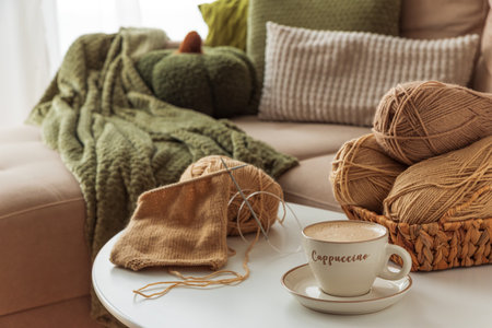 Cozy Living Room with Yarn, Pumpkins, Pillows and Cup of Cappuccino on White Tableの写真素材