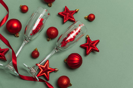 Champagne Flutes with Red Christmas Ornaments and Ribbon on Green Backgroundの写真素材