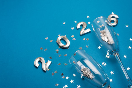 New Year 2026 Champagne Flutes with Silver Confetti on Blue Background