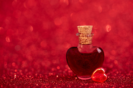 Heart-Shaped Glass Bottle with Red Liquid on Glittery Background for Valentines Day Celebrationの写真素材