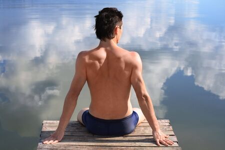 A man is sitting at the water where the blue sky is mirroredの写真素材