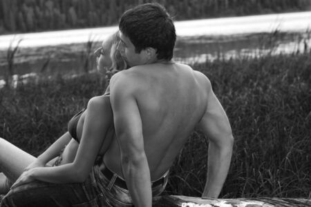a man and a woman in tender pose sitting on the log (black and white picture)の写真素材