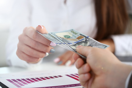 Male arm pay bunch of hundred dollars bills to office clerk closeup. Bribery accept backhander banknote venality laundering back scheme offshore company is kickback collusion lobby gift compensationの写真素材