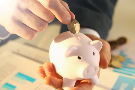 Hand businessman putting pin money into pig. Future needs loan education or mortgage credit spend vacation of dream effective buying financial risk and safety conceptの写真素材