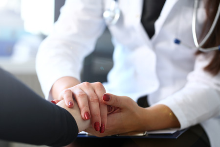 Young female doctor holds sick patient by hand expressing condolences and sympathy reports bad news about loss of loved ones due to cancer deadly aids disease and says we can handle support concept.の写真素材