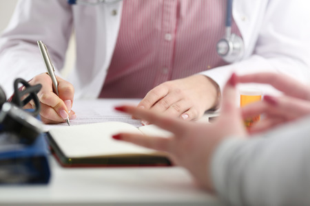 Female medicine doctor hand hold jar of pills and write prescription to patient at worktable. Panacea and life save, prescribing treatment, legal drug store concept. Empty form ready to be usedの写真素材