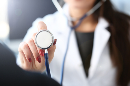 Beautiful smiling female doctor hold in arm stethoscope head going to listen patient. Tool shop or store physical disease prevention er consultant 911 pulse measure healthy lifestyle conceptの写真素材