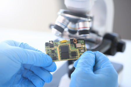 An employee of computer repair service assembly keeps spare part motherboard processor in hands gloves for installation by method soldering technology developmentの写真素材