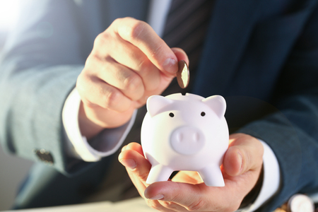 Hand businessman putting pin money into pig. Future needs loan education or mortgage credit spend vacation of dream effective buying financial risk and safety conceptの写真素材