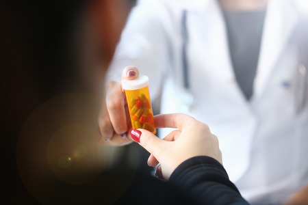 Female medicine doctor hand hold jar of pills and write prescription to patient at worktable. Panacea and life save prescribing treatment legal drug store concept.の写真素材