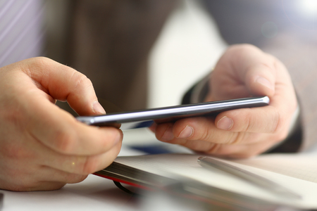 Male arm in suit hold phone and silver pen at workplace closeup. Read news mania send sms chat addict use electronic bank modern lifestyle job plan colleague share blog tweet web application searchの写真素材