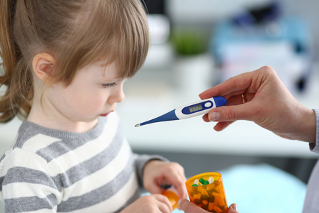 Female hand holding thermometer measuring sick little girl closeupの写真素材