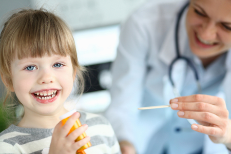 Cute smiling happy little girl hold in hand bottle of tablets at doctor office portraitの写真素材
