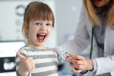 Cute little girl at doctor office showing respect gratitude and approve for quality service with thumb up gesture portraitの写真素材