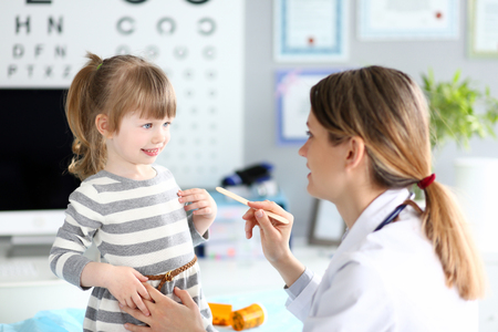 Female paediatrician examining little kid patient throat with wooden stickの写真素材
