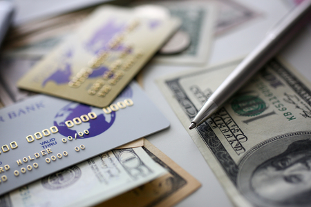 Banking plastic card and silver pen lying on big amount of US moneyの写真素材
