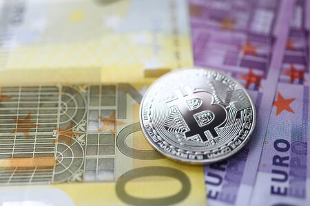 Silver bitcoin with euro cash lie on the table