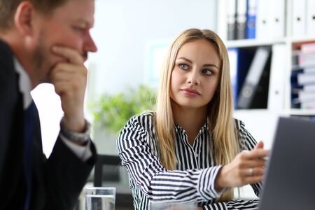 Beautiful blonde secretary sitting at workplace talking with bossの写真素材