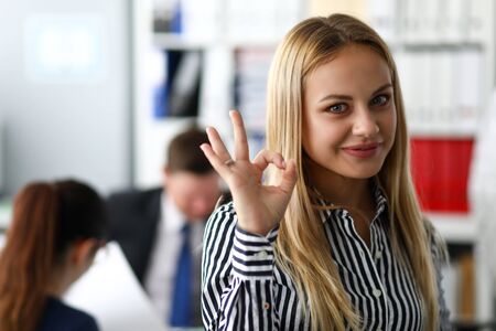 Smiling female clerk showing OK or confirm sign with her armの写真素材