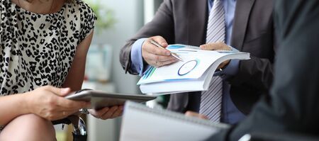Focus on smart businessman pointing at biz statistics. Businesspeople sitting in corporation conference room and discussing new start-up. Business meeting concept. Blurred backgroundの写真素材